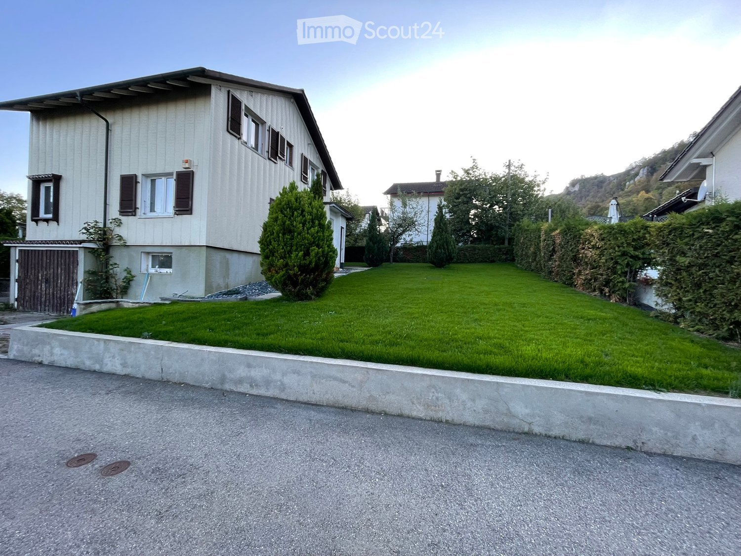 Two-story house with beige siding, multiple windows with shutters, garage, and well-maintained lawn.