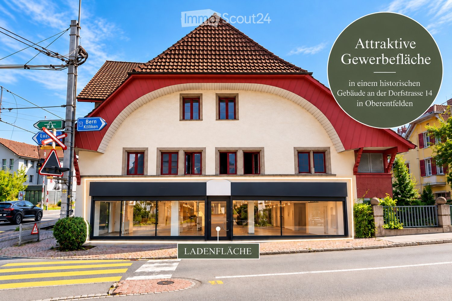 A two-story commercial building with a red and white facade, large windows, and a modern storefront. The building is situated on a street with signage for directions to Bern and Luzern.