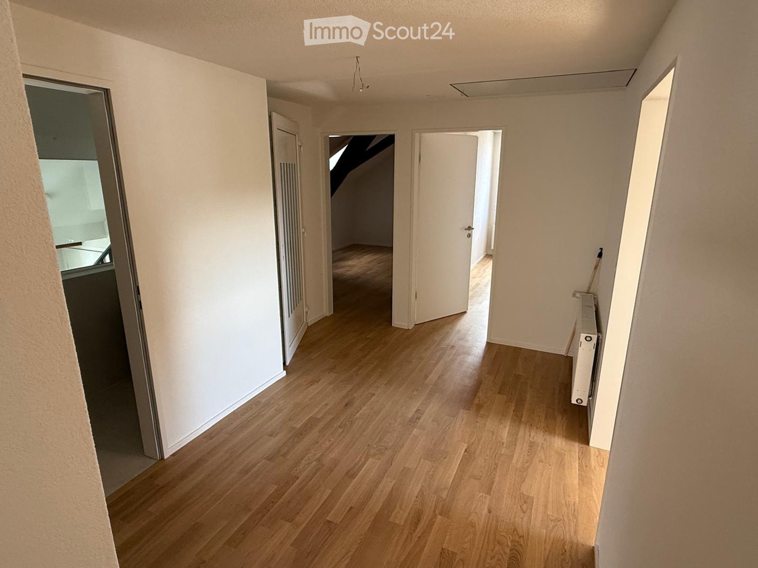 Empty hallway with wooden flooring, white walls, and several open doors leading to other rooms.