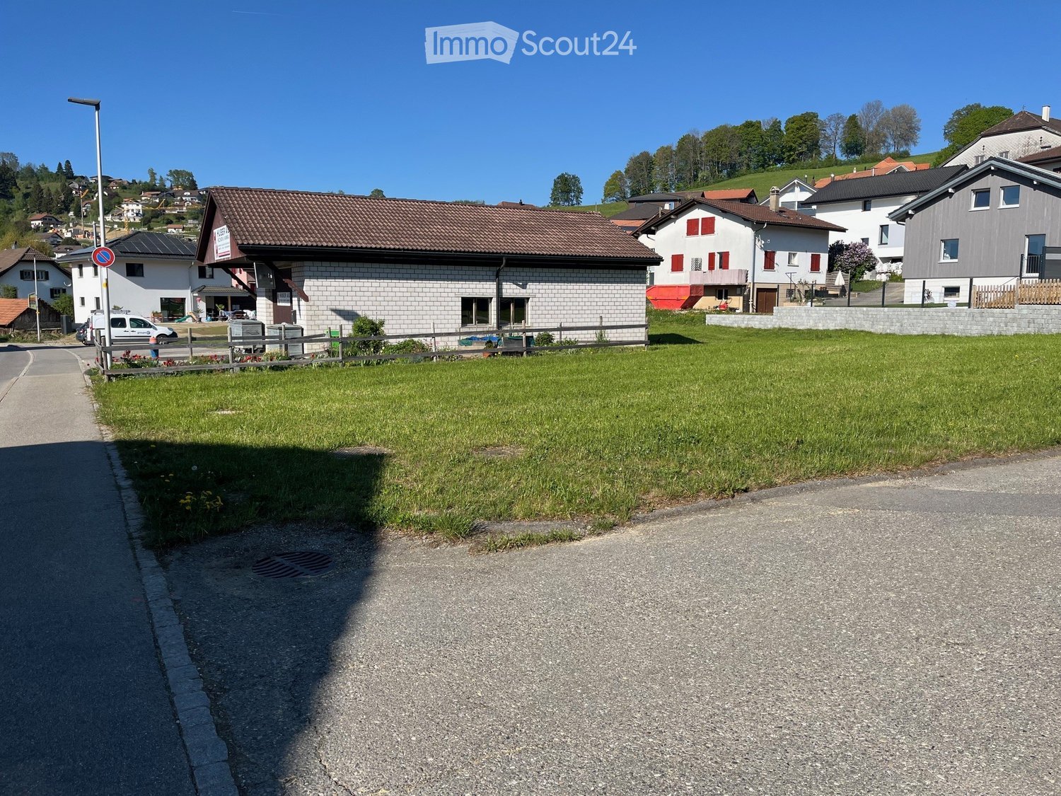 Residential street with several houses, green lawn, and a clear blue sky.