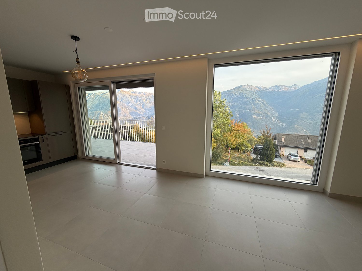 Empty room with large windows offering a scenic mountain view, tiled floor, and sliding glass doors leading to a balcony.