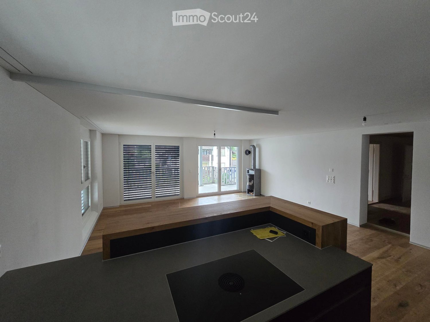 Modern, minimalist room with a dark countertop, wooden bench seating, and a small fireplace. Large windows and sliding glass doors lead to a balcony area.