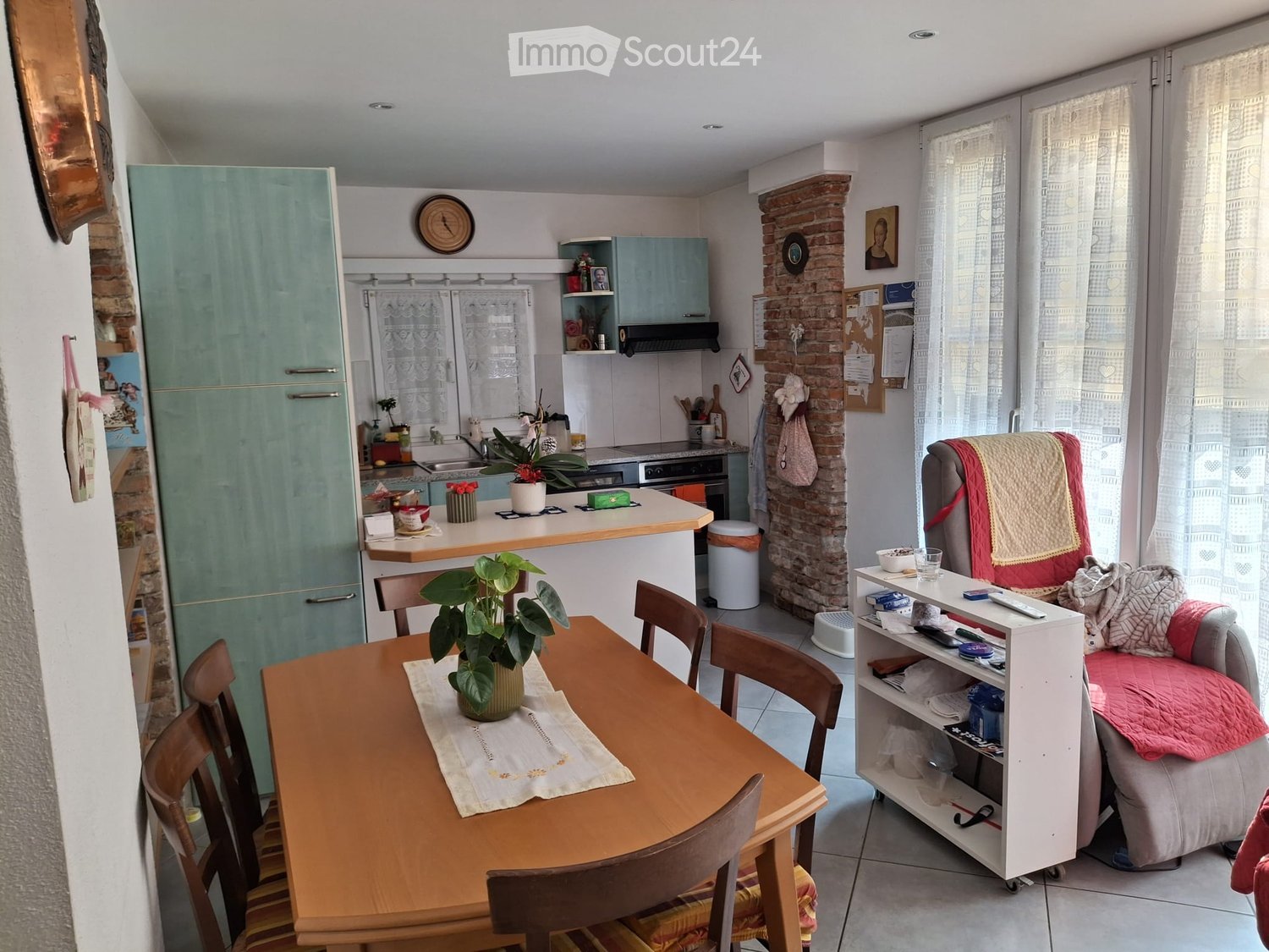 A well-lit living and dining area with a sofa, dining table, chairs, kitchen appliances, and a brick accent wall.