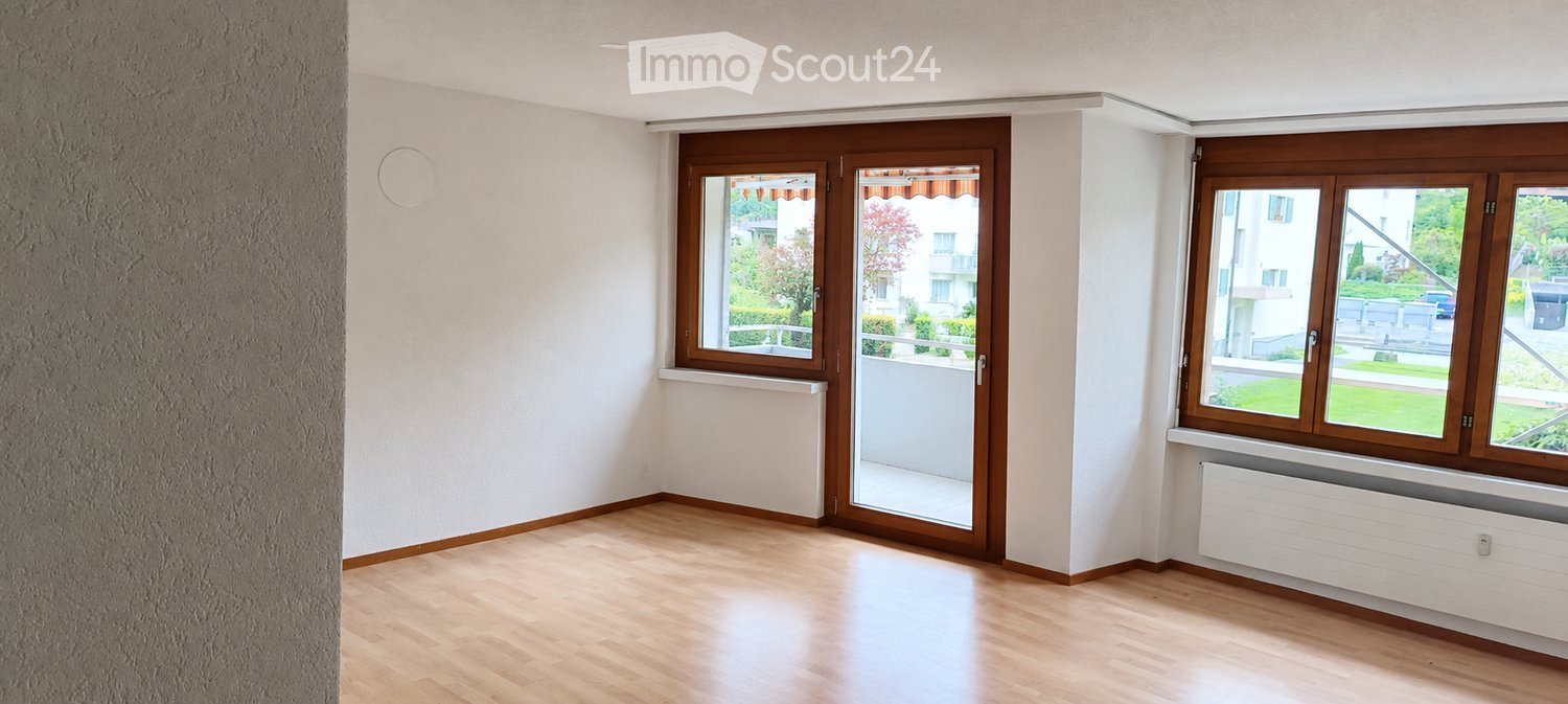 Empty room with wooden flooring, white walls, large windows, and a sliding glass door leading to a balcony.