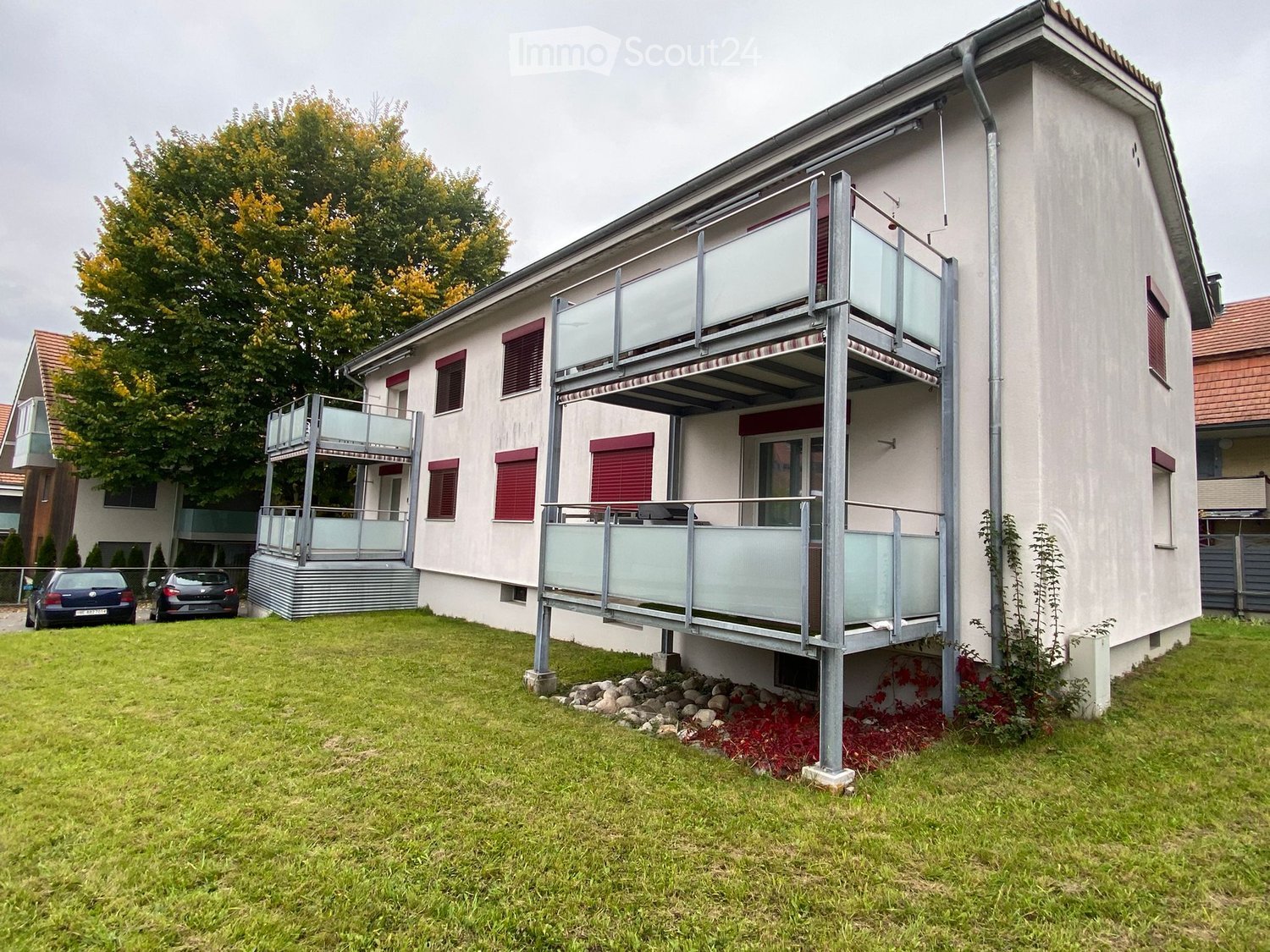 2 story building, 2 balconies, red shutters, white exterior, tree, cars parked