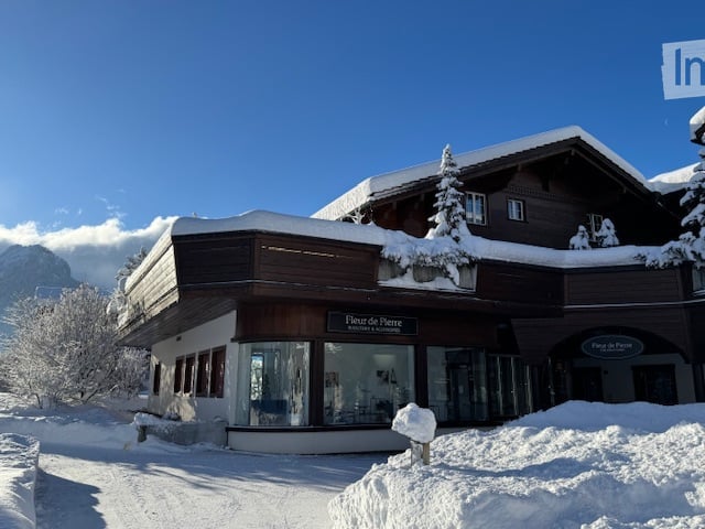 A large, multi-story wooden building with snow-covered roof and surrounding snow-covered trees, likely a ski lodge or resort.