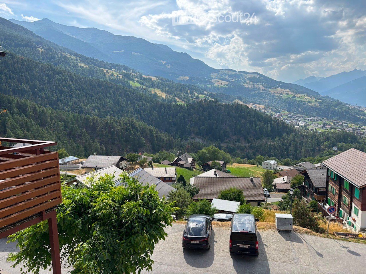 Panoramic view of a valley with houses, trees, and mountains in the background.