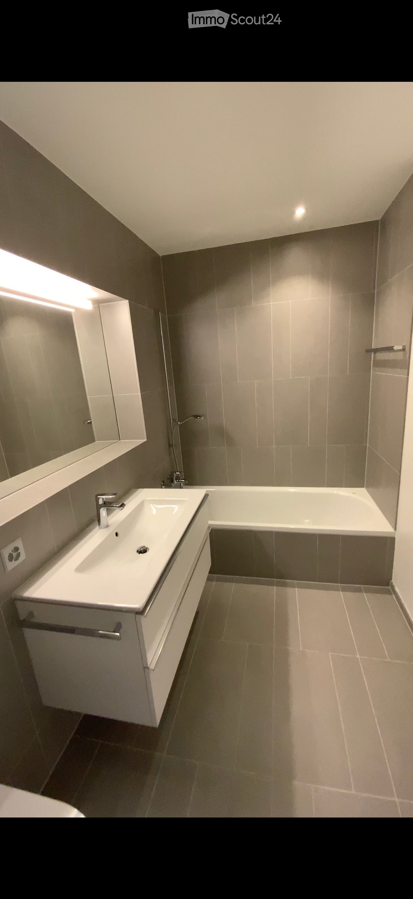 Modern bathroom with a white sink, bathtub, and mirrored cabinet. Features sleek fixtures and neutral tones.