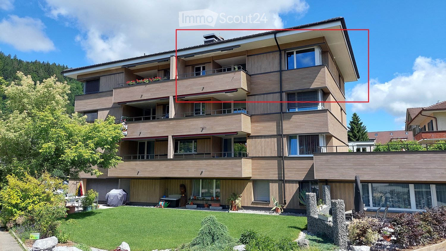 Modern multi-story building with balconies, large windows, and a well-maintained garden area.