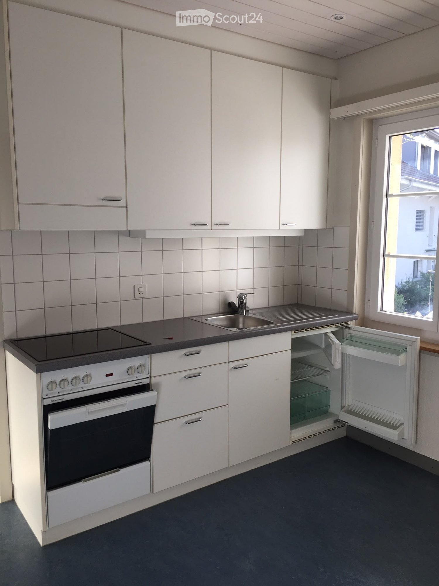 Modern kitchen with white cabinets, stainless steel sink, oven, and refrigerator. The refrigerator door is open, revealing shelves inside.