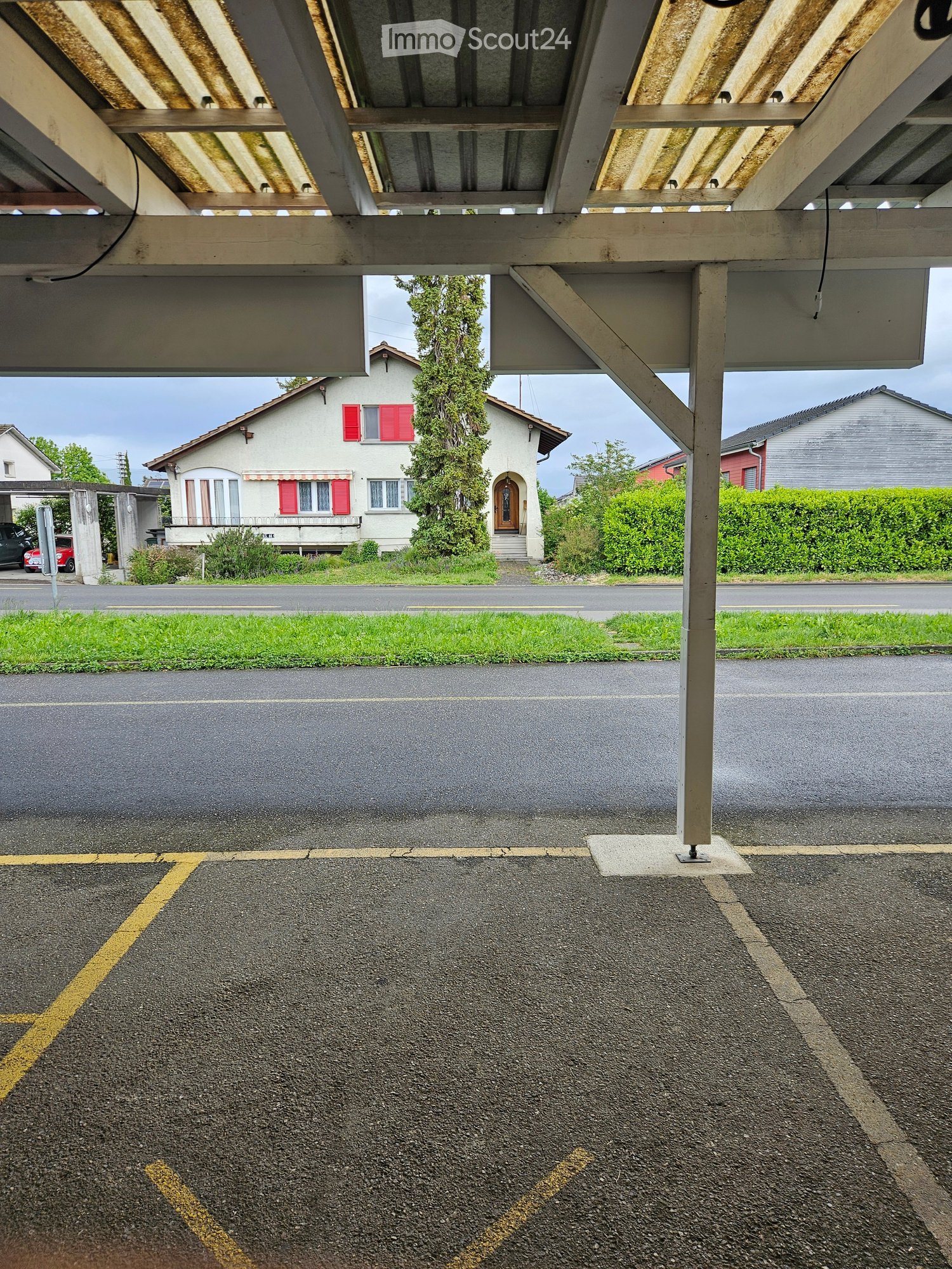 Residential building with a covered parking area, visible parking spaces, and a small garden area.