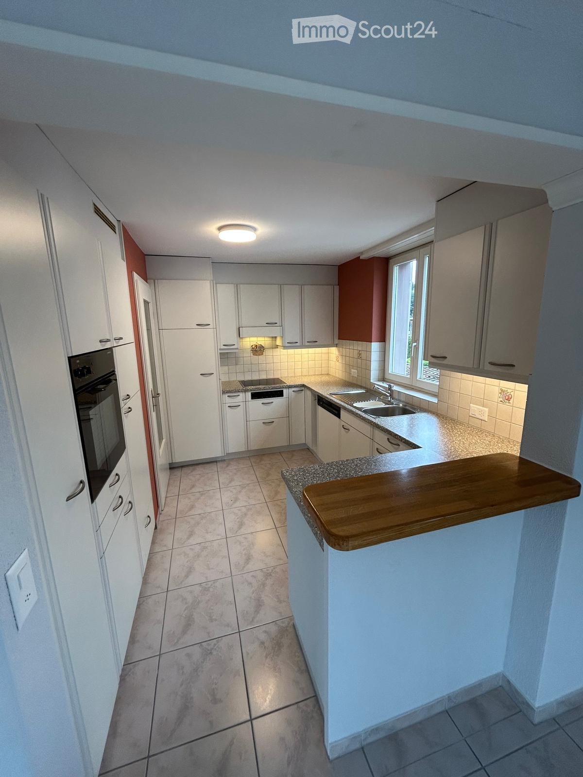 Modern kitchen with white cabinets, granite countertop, sink, oven, dishwasher, and a wooden breakfast bar.