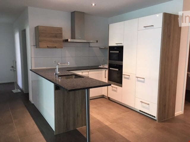 Modern kitchen with white cabinets, wooden accents, a central island with a sink, and built-in ovens.