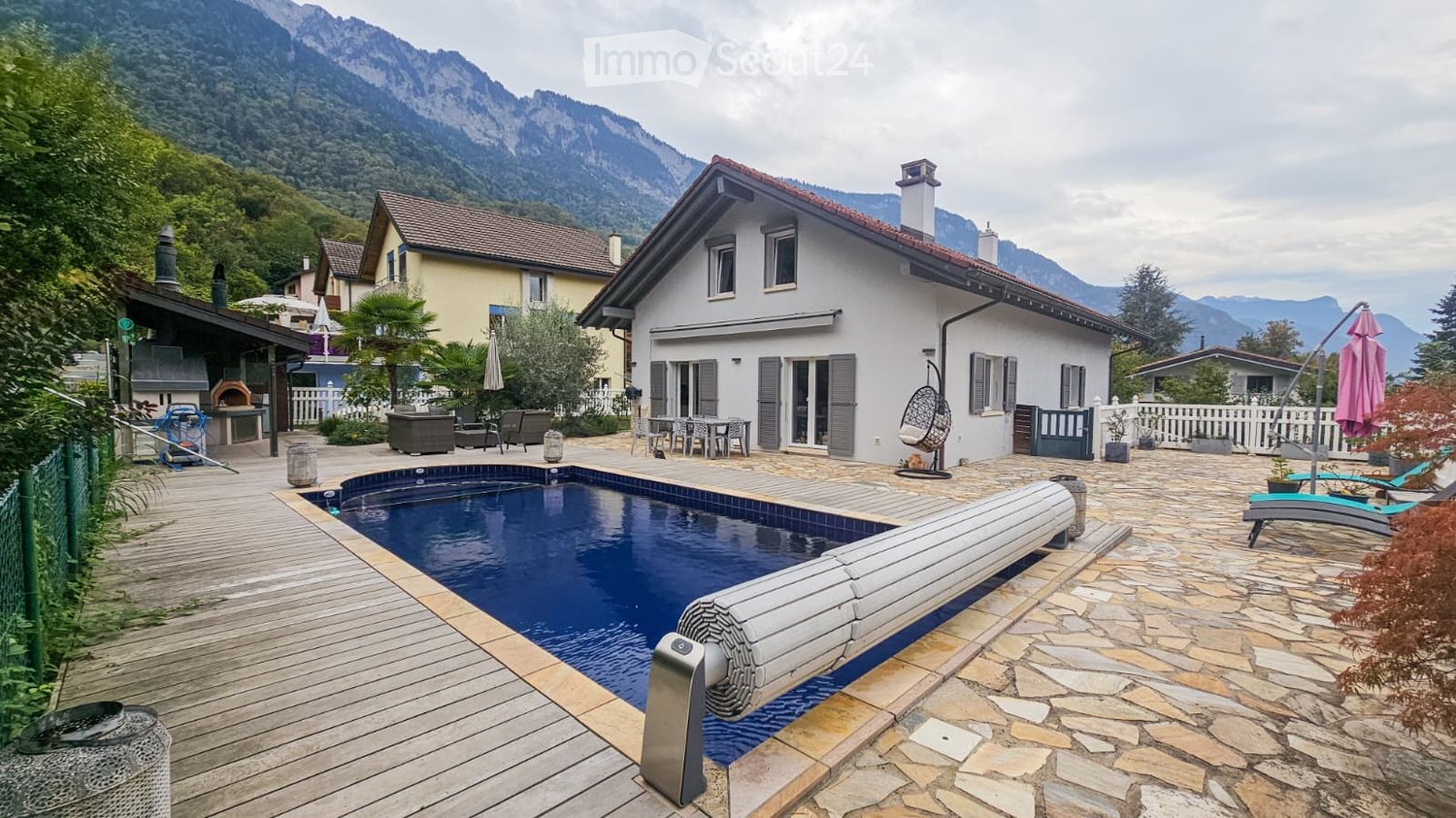 Outdoor area with a swimming pool, wooden decking, lounge chairs, and a view of mountains.