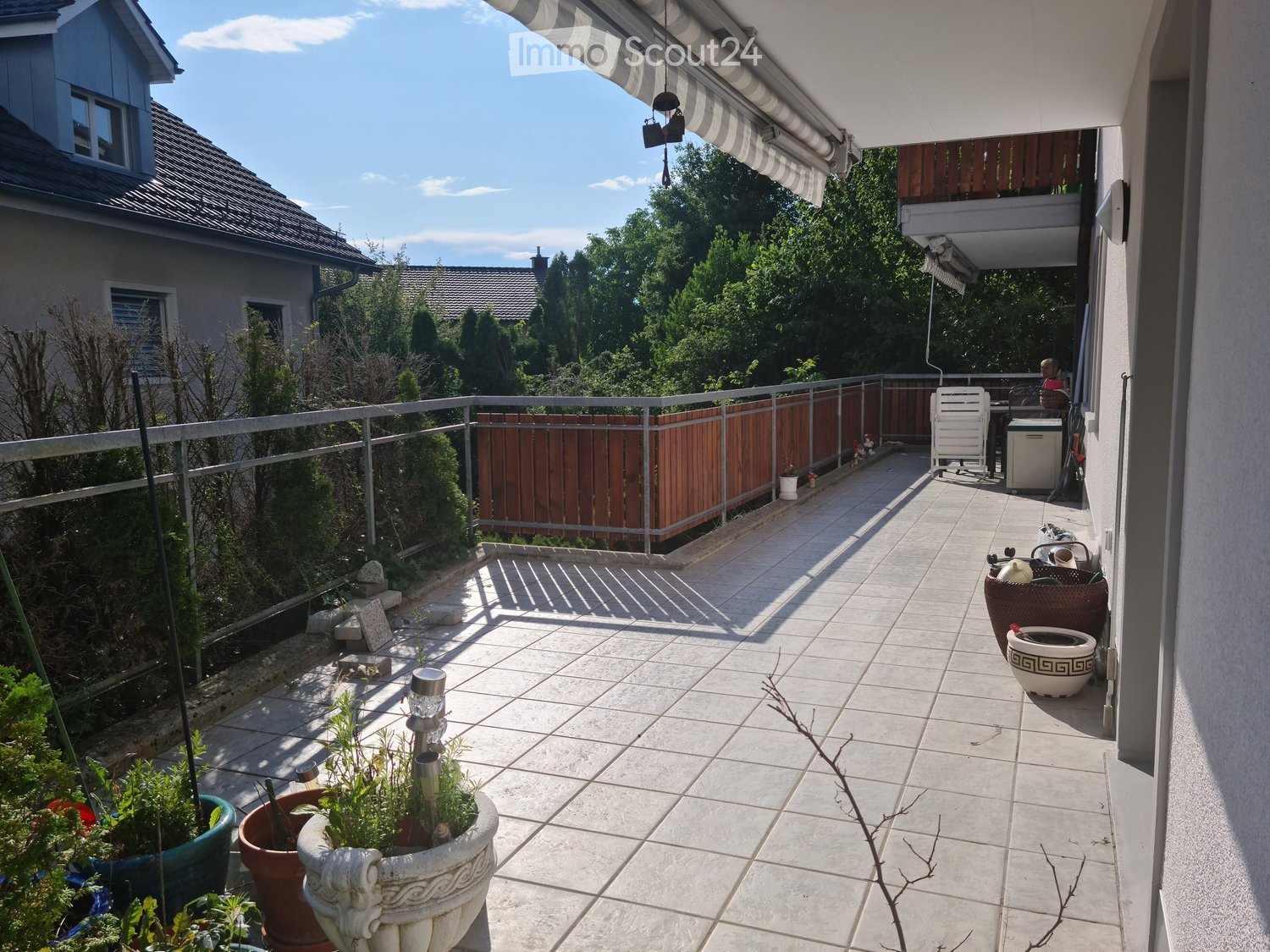 Balcony with tiled floor, metal railing, potted plants, and a small table and chair set.