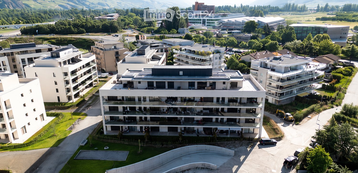 Aerial view of a modern residential complex with multiple apartment buildings, surrounded by greenery and a scenic mountain backdrop.