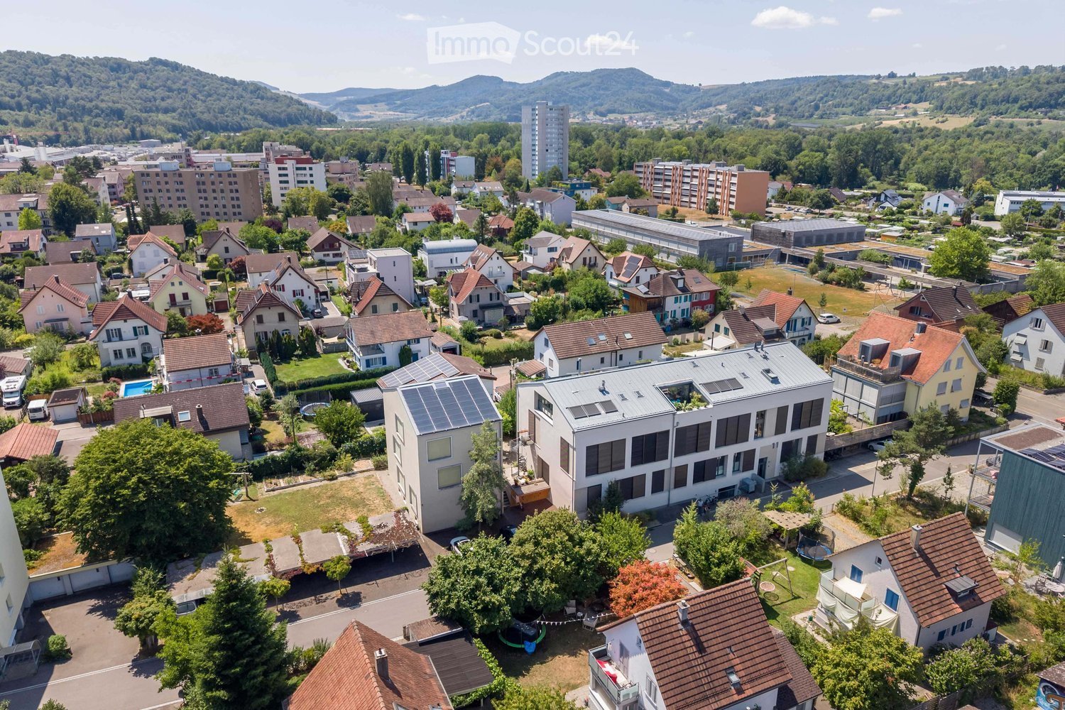 Aerial view of a suburban neighborhood with single-family homes, apartment buildings, and green spaces, surrounded by hills and trees.