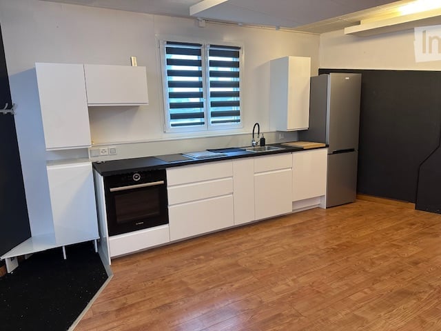Modern kitchen with white cabinets, black countertop, stainless steel sink, and appliances.