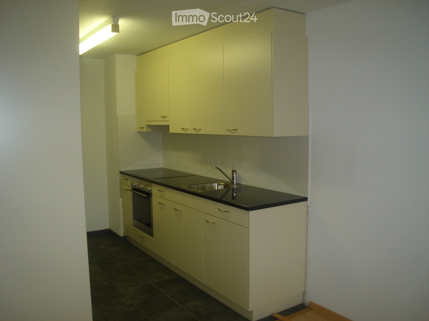 Compact kitchen with light-colored cabinets, black countertop, stainless steel sink, and built-in oven.