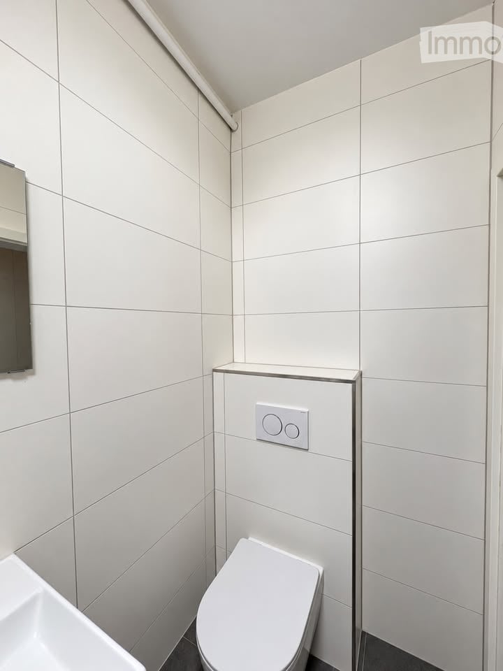 Modern bathroom with white tiled walls, a toilet, a sink, and a mirror. The space is clean and contemporary with a sleek design.