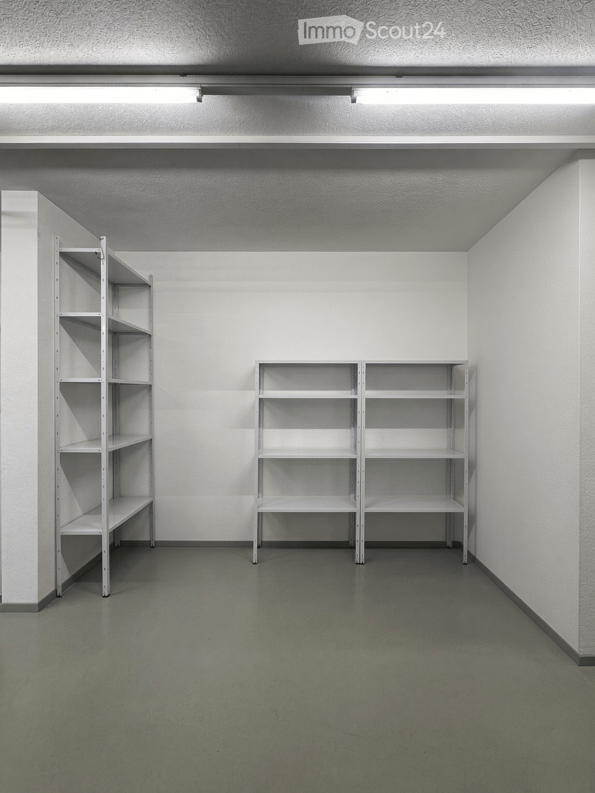 Empty room with white walls, grey floor, and two white metal shelving units.