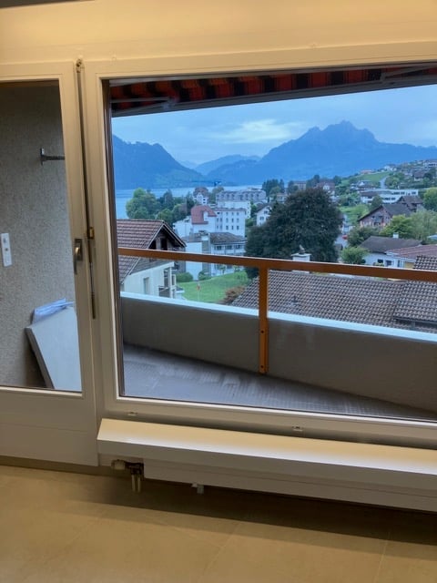 Balcony with large windows offering a scenic view of mountains and a lake, with a wooden floor and white railings.