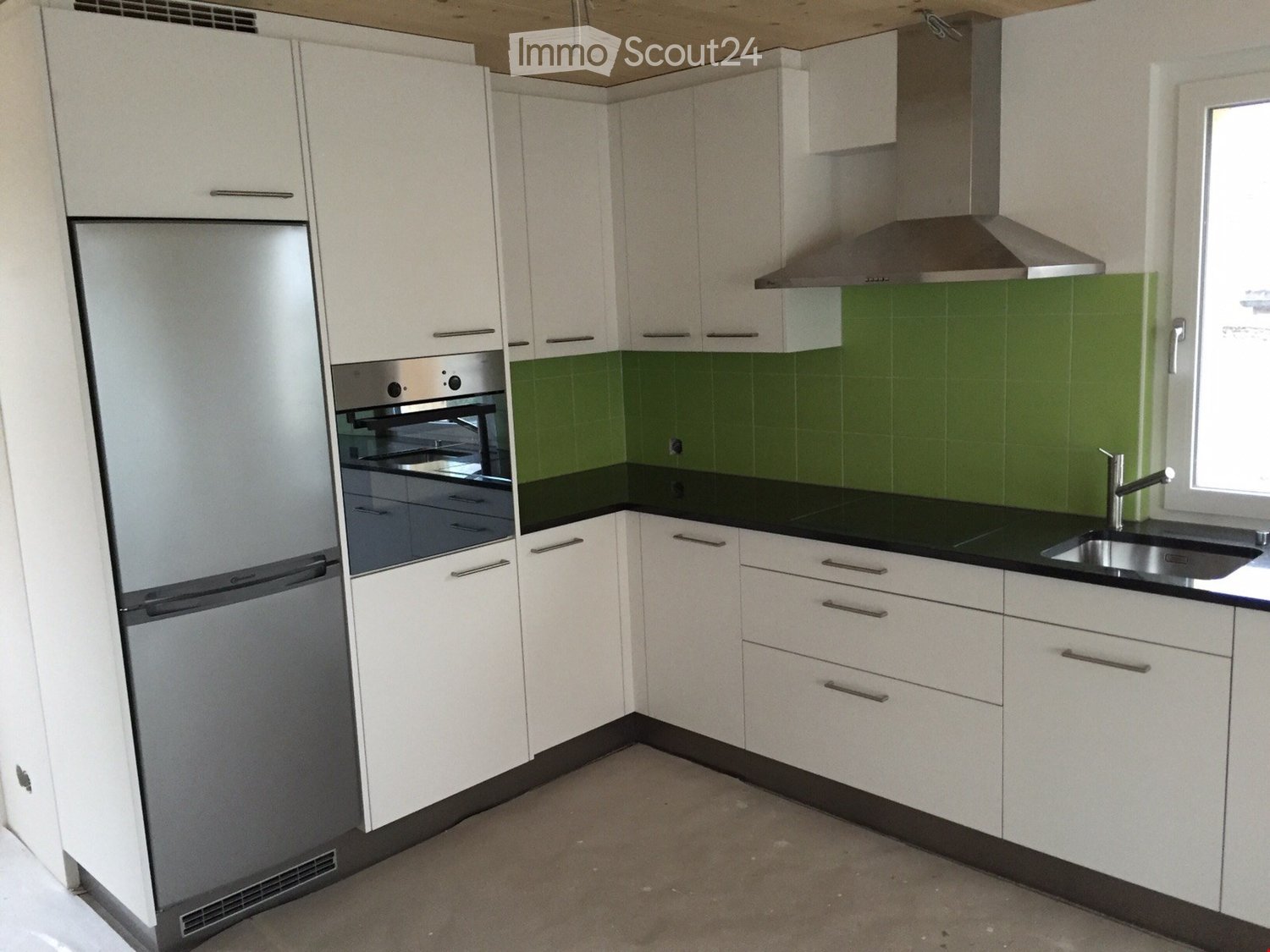 modern kitchen with white cabinets, green tiled backsplash, stainless steel appliances, black countertops, and a stainless steel range hood
