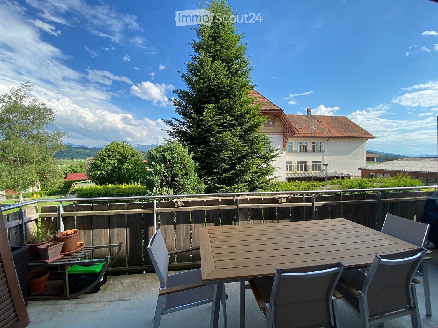 wooden table and chairs, metal railing, potted plants, view of a house and trees