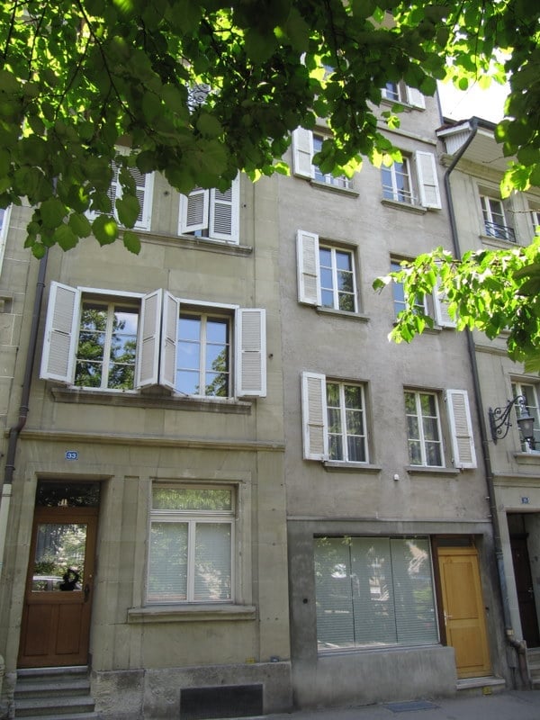 Four-story residential building with light-colored stone facade, multiple windows with shutters, and a wooden front door.