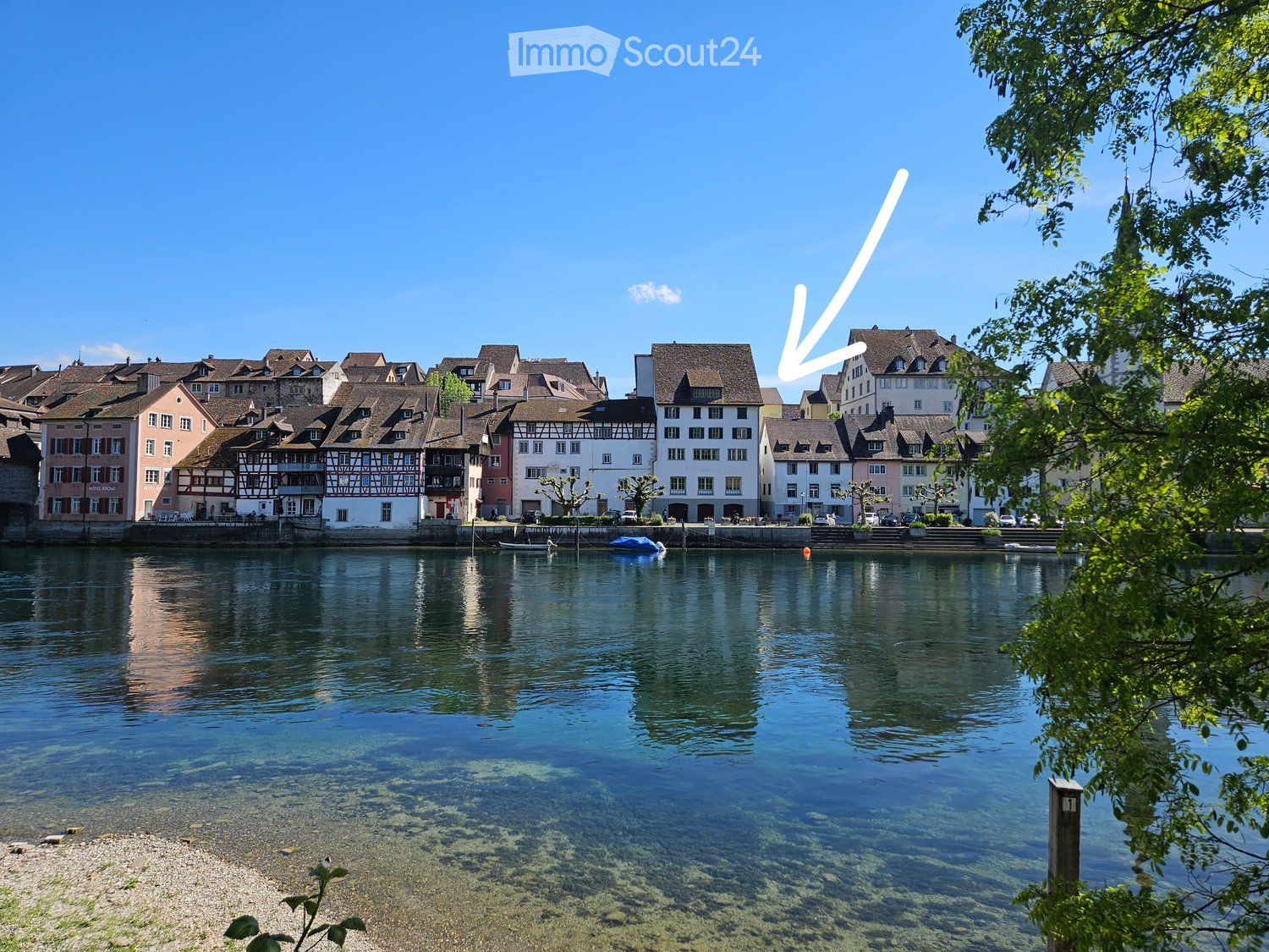 A picturesque town with traditional houses along a calm river, featuring a mix of architectural styles and a clear blue sky.