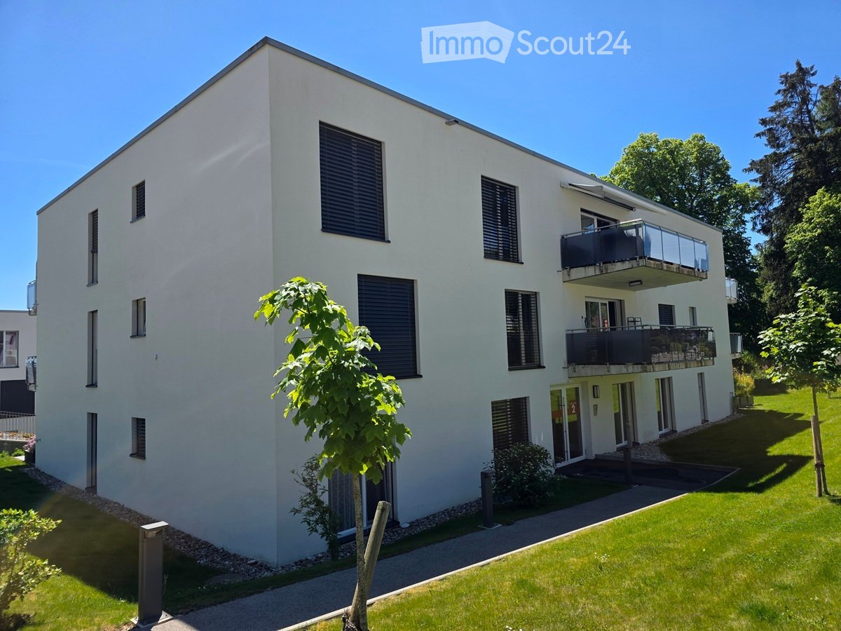 Modern two-story white building with multiple windows, balconies, and a small garden area.