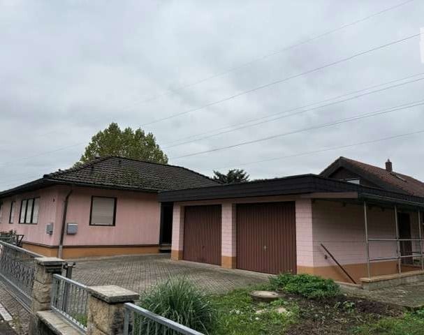 Single-story house with pink exterior, two garage doors, and a small garden area.