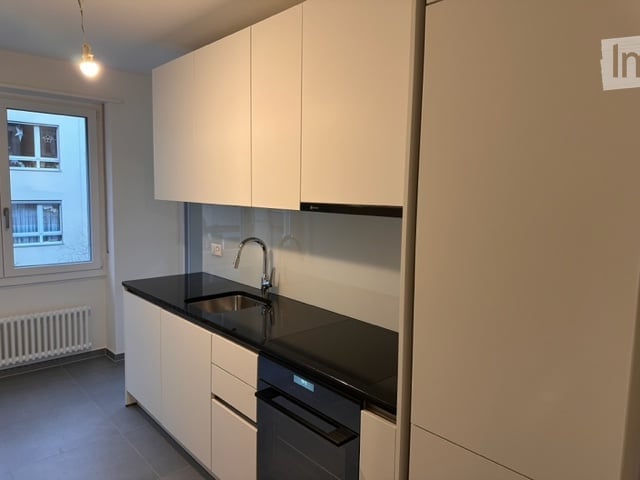 Modern kitchen with white cabinets, black countertop, stainless steel sink and faucet, and built-in dishwasher.