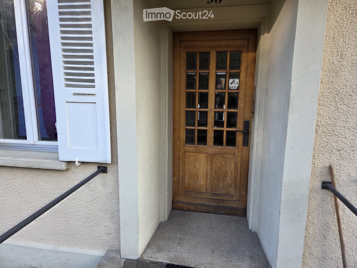Wooden front door with glass panels, white louvered window, and a small CCTV sign above the door.