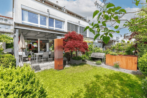 Well-maintained garden area with a lawn, patio seating, and decorative elements like a wooden bench and a red sculpture.