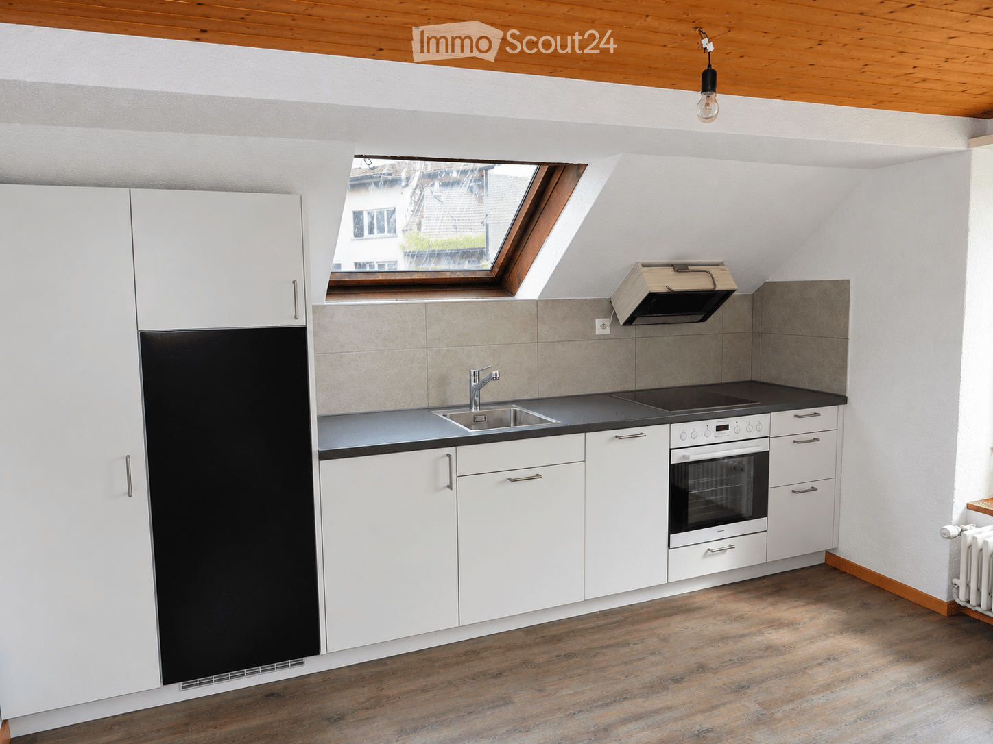 Modern kitchen with white cabinets, black countertop, stainless steel sink, oven, and refrigerator. Features a skylight window and wooden flooring.