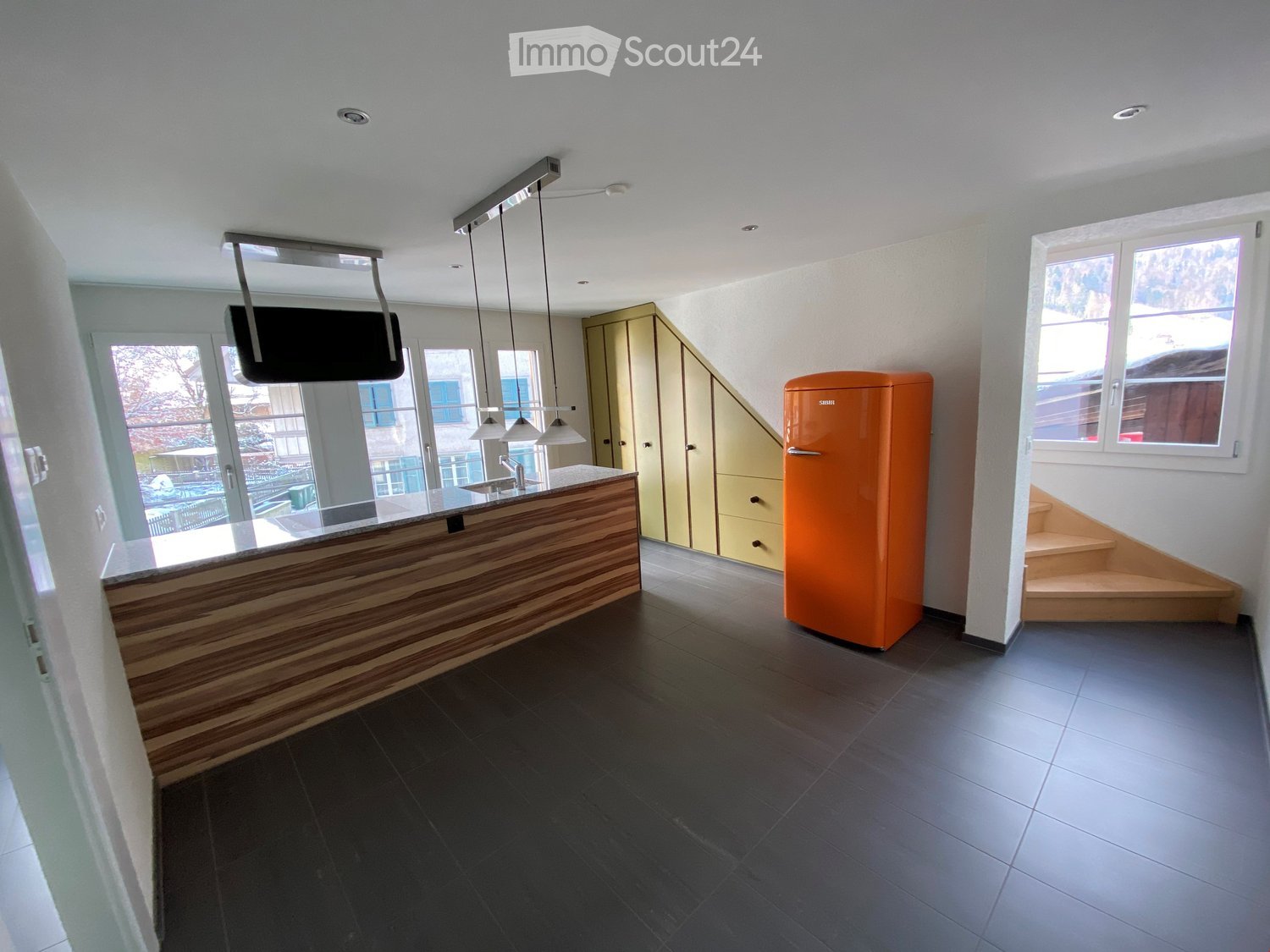 Modern kitchen with dark tiled floor, wooden counter, orange refrigerator, and built-in cabinets.