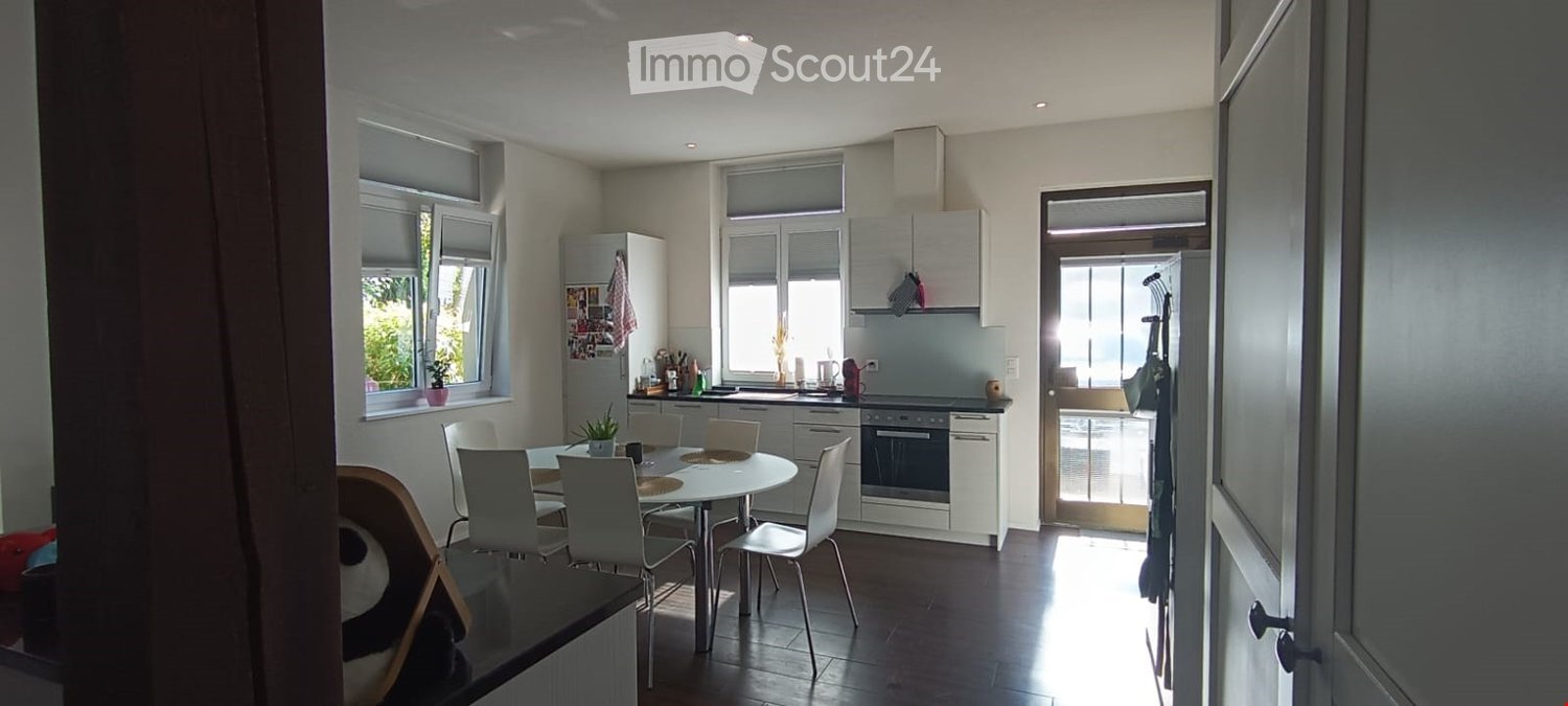 Bright, modern kitchen and dining area with white cabinets, stainless steel appliances, a round dining table with six chairs, and large windows letting in natural light.