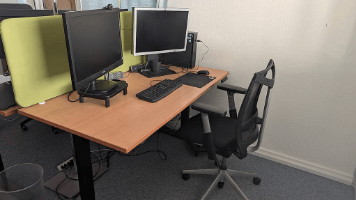 Office space with a wooden desk, ergonomic chair, dual monitors, keyboard, and mouse.