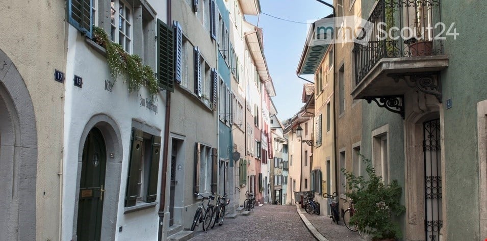 Narrow cobblestone street lined with colorful buildings, featuring bicycles parked along the sides and small balconies with potted plants.