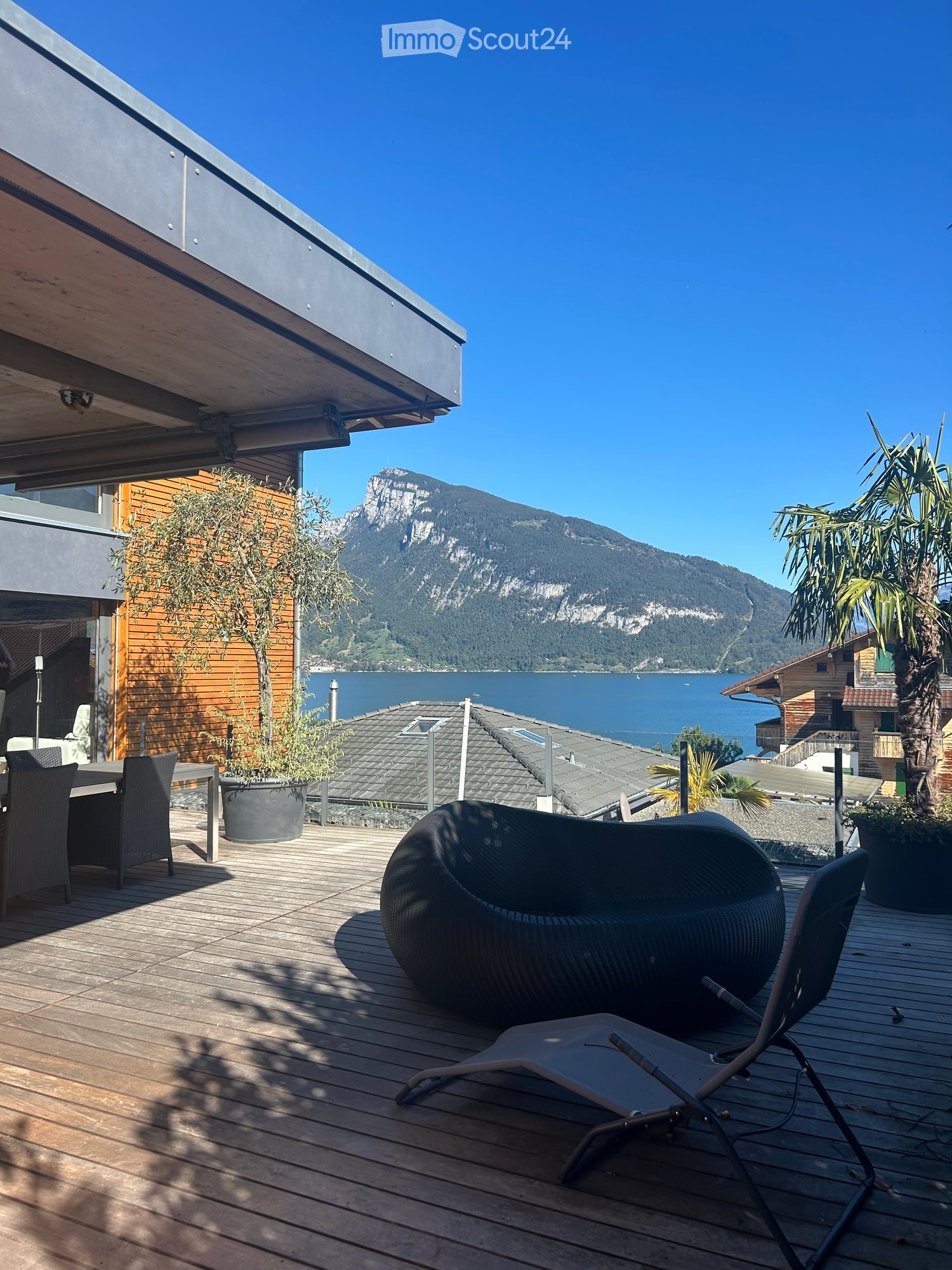 Wooden terrace with outdoor furniture, overlooking a lake and mountain view.