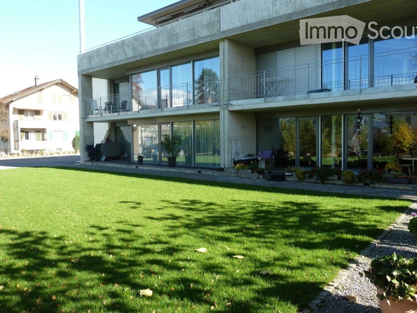 2 story house, large glass windows, concrete walls, balconies, lawn with plants
