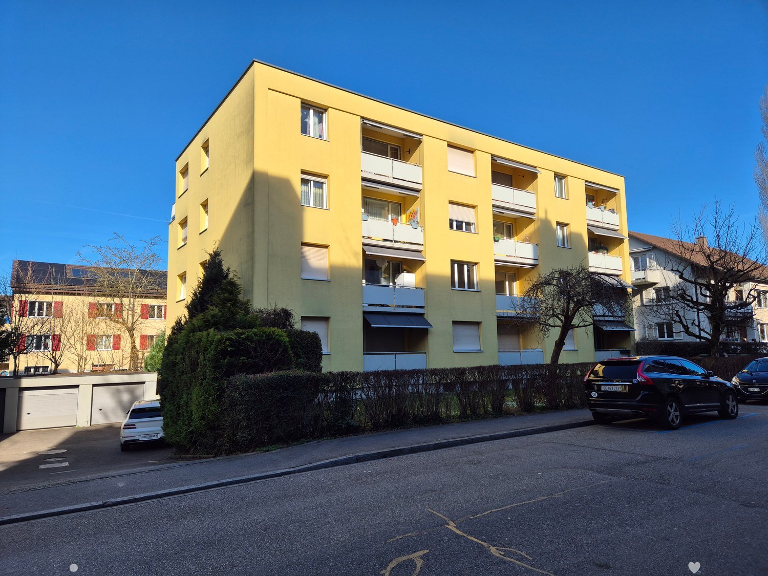 Yellow building, balconies, windows, trees, parked cars, concrete road