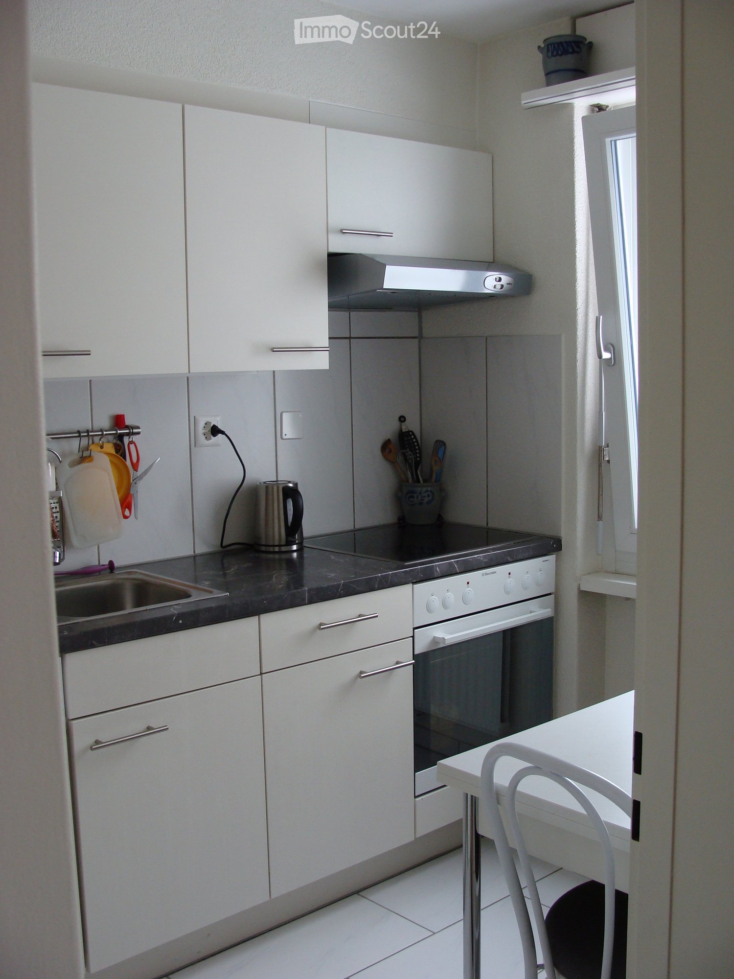 white kitchen with marble counter top, sink, electric kettle, stove, and oven, white cabinets, white table, chairs