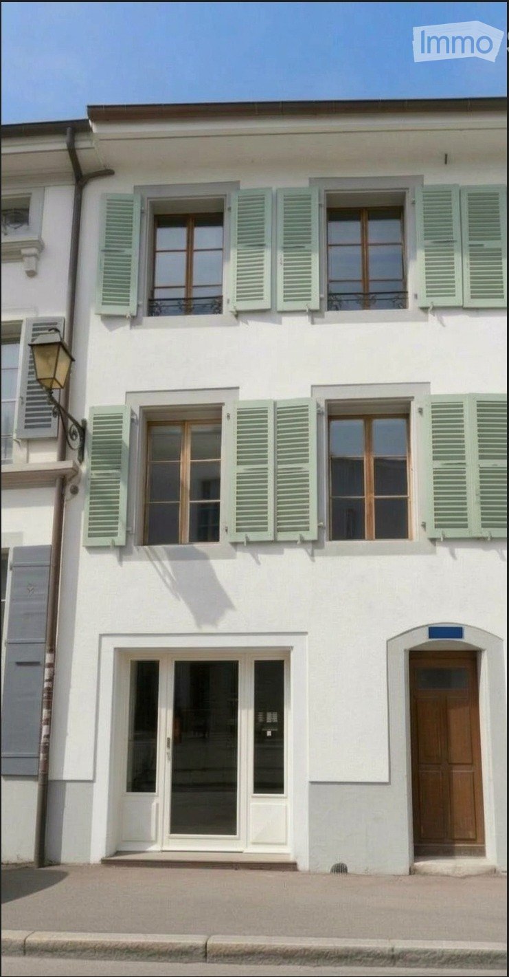 A two-story white building with green shutters, large windows, and a wooden front door.