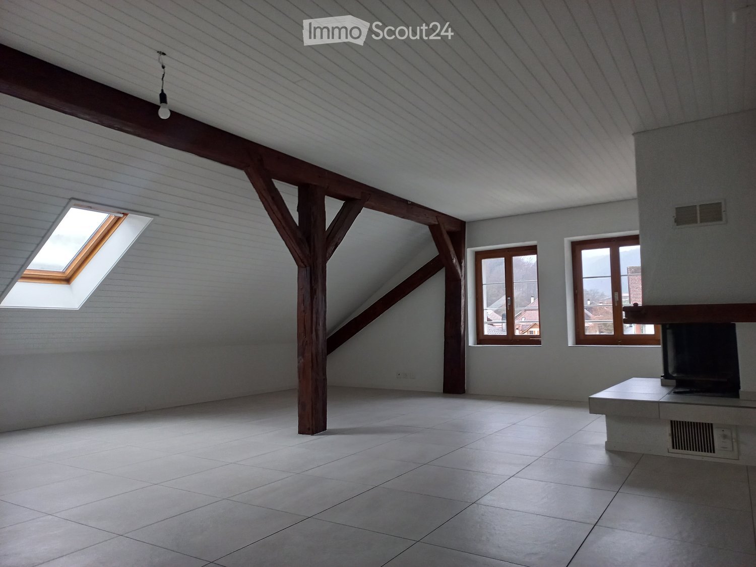 Empty attic space with wooden beams, skylight, and windows, featuring tiled flooring and exposed wooden beams.