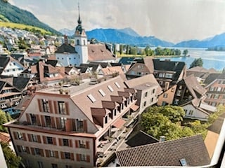 A picturesque town view with traditional European architecture, including a prominent church tower, red-roofed buildings, and a serene lake in the background.