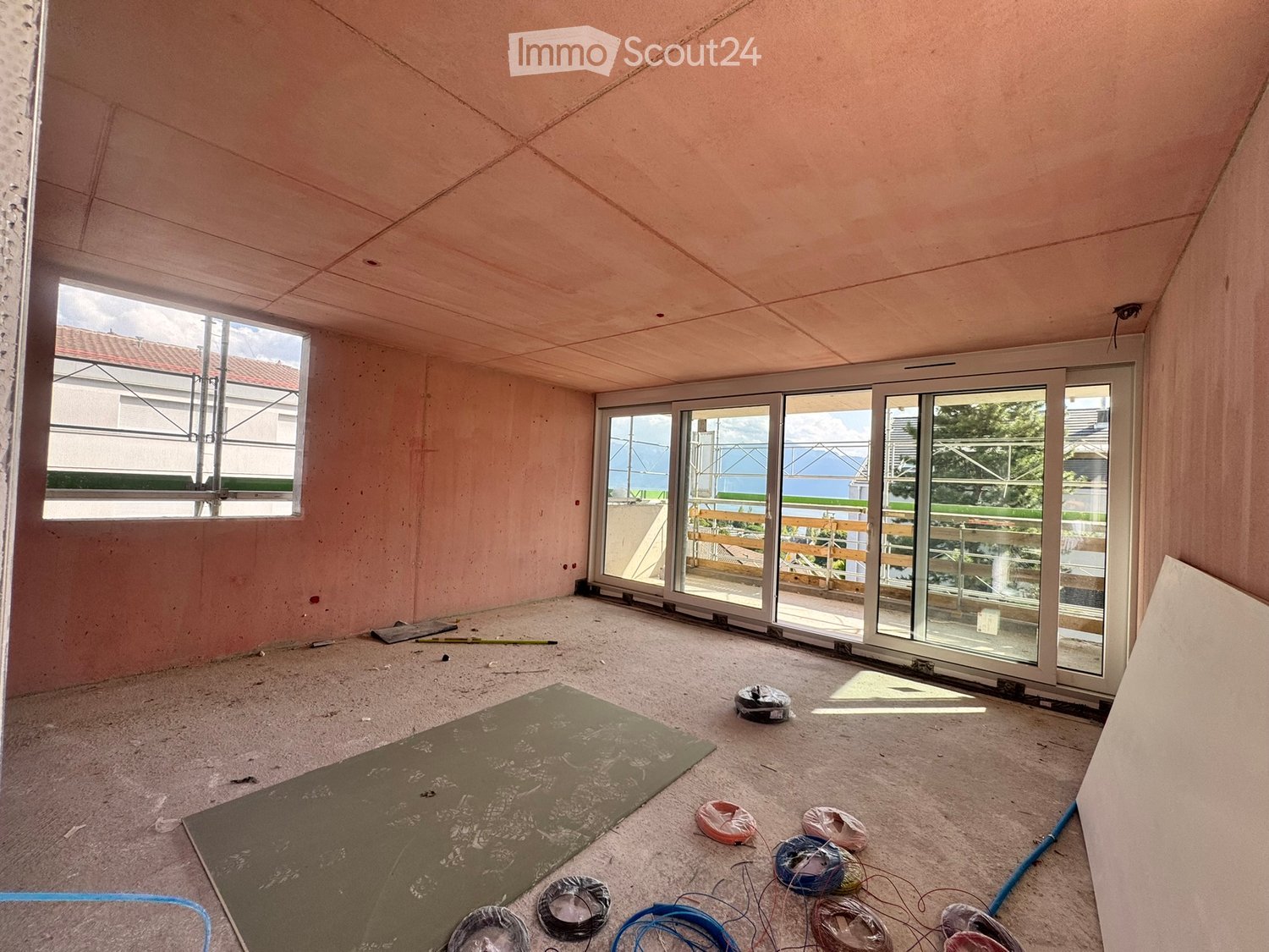 Empty room with unfinished walls and floor, large windows, and a sliding glass door leading to a balcony area.