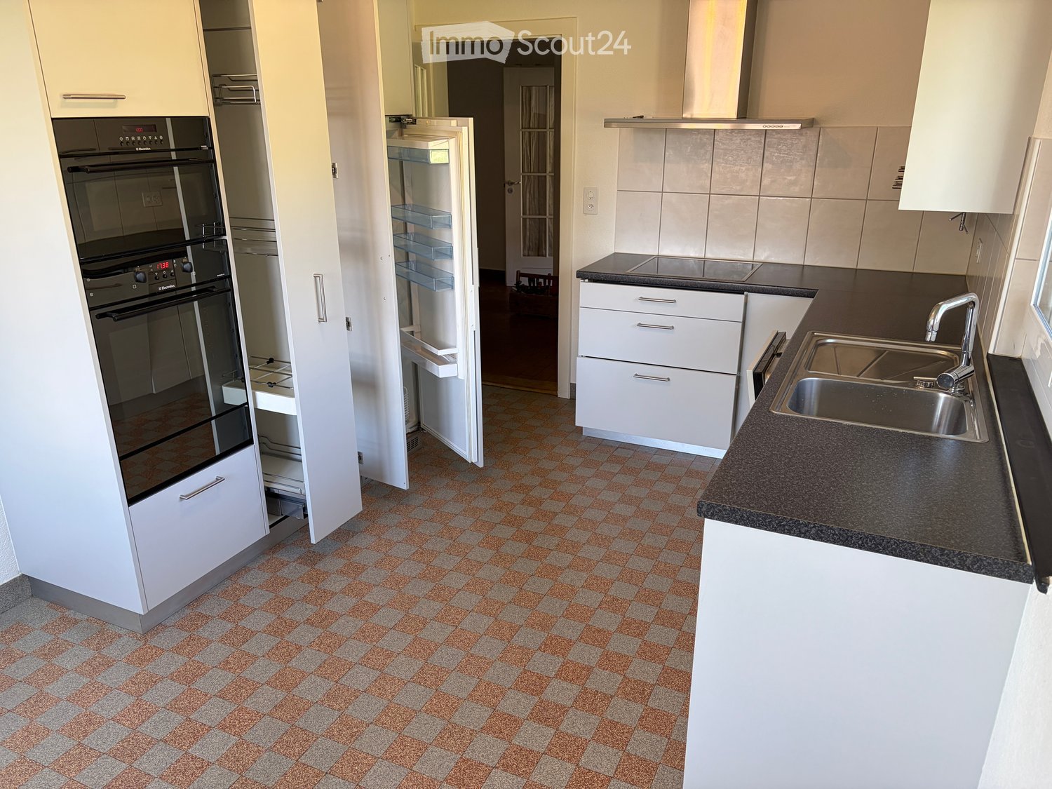 Modern kitchen with white cabinets, black countertops, a stainless steel sink, and an oven. The floor features a checkered tile pattern in orange and gray.