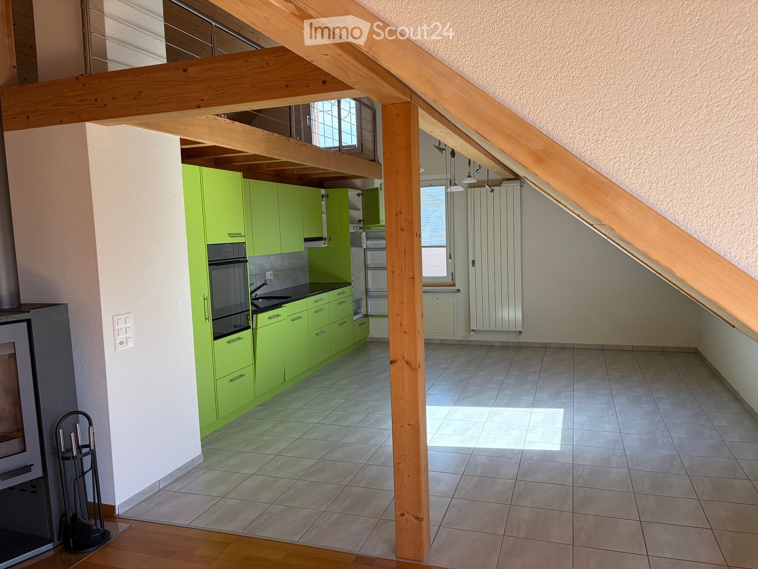 Bright kitchen with green cabinets, stainless steel oven, sink, and radiator. Wooden beams and tiled floor.